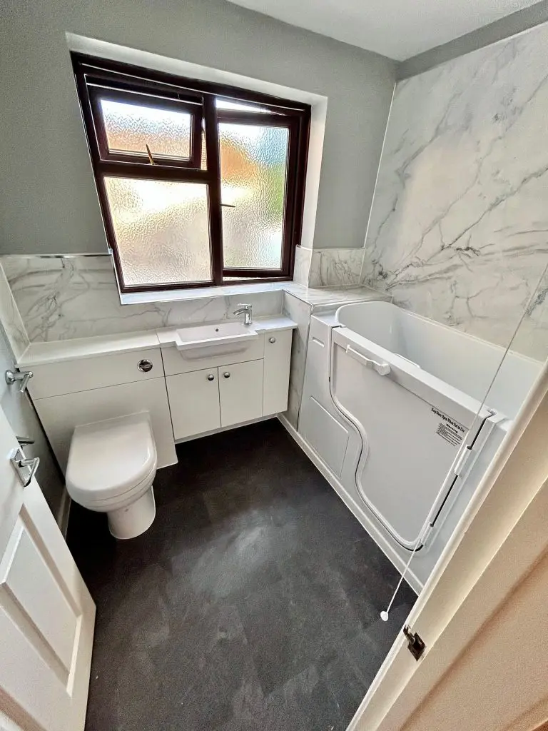 A bathroom with sink, toilet, and a walk in bathtub.